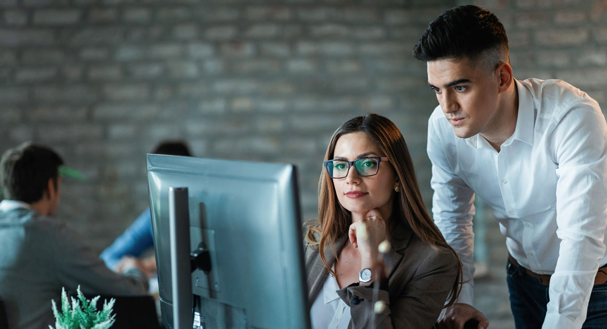 Two professionals analyzing data on a computer screen in a modern office setting.